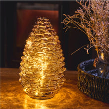 Amber glass pinecone light with 15 warm white LEDs illuminated on a table